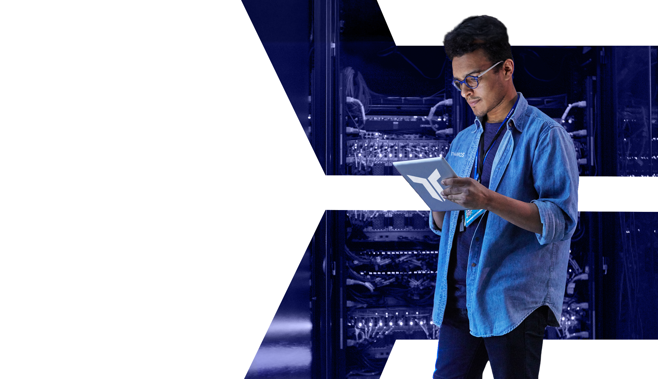 man wearing a jean button up shirt and a Tharros lanyard types on a tablet in a server room