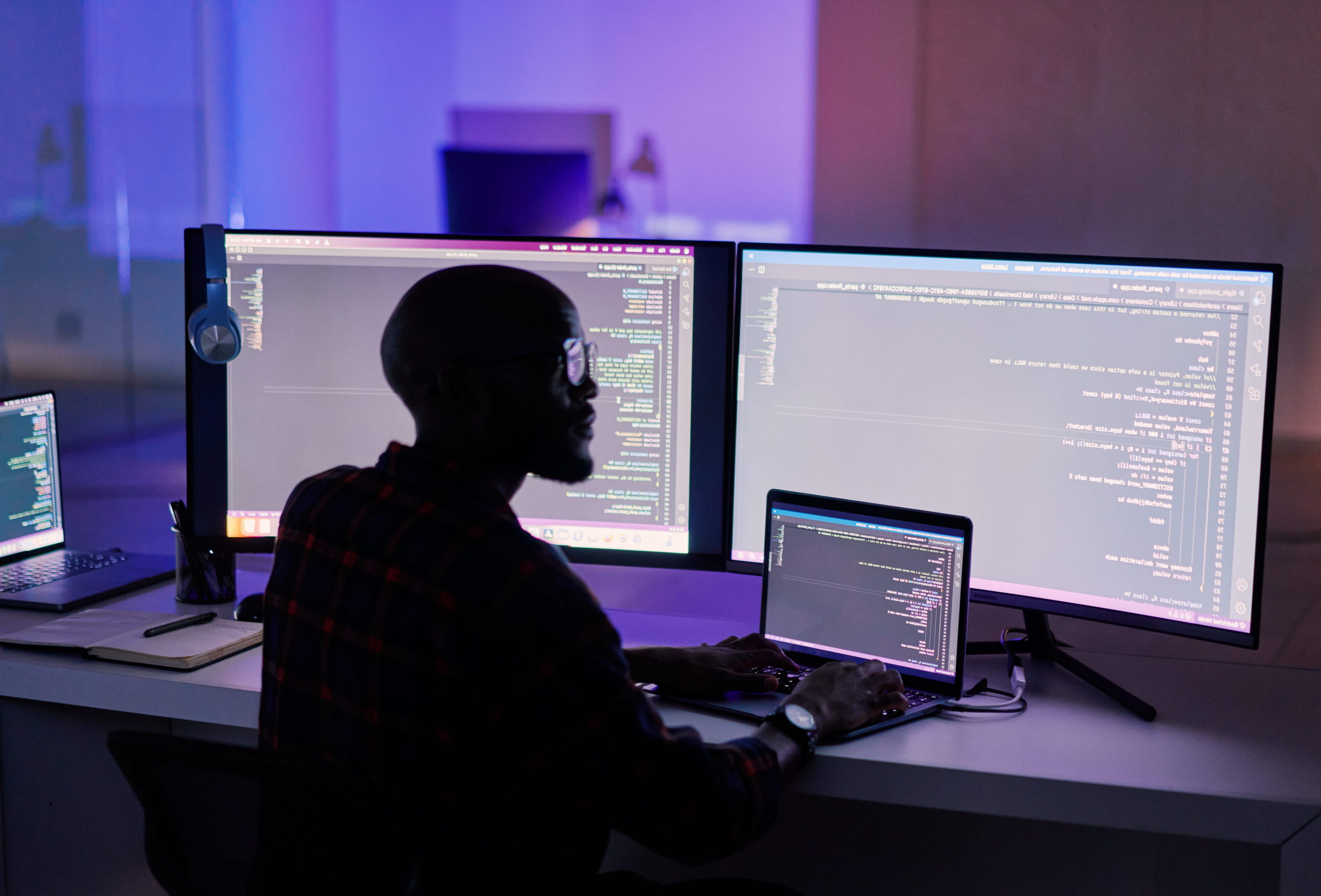 man works at his computer with 3 monitors at night in a dark room