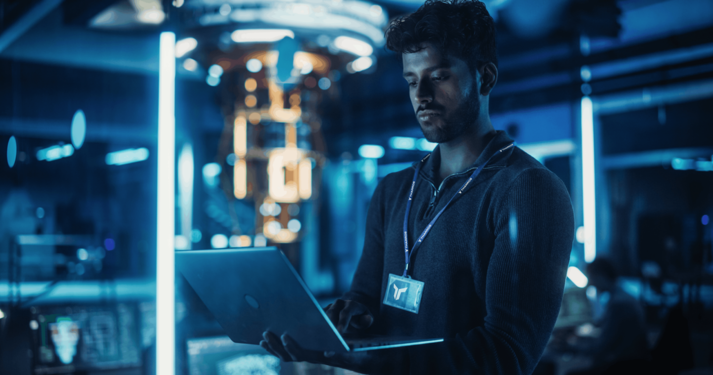 man wearing tharros lanyard looks at laptop in a tech lab